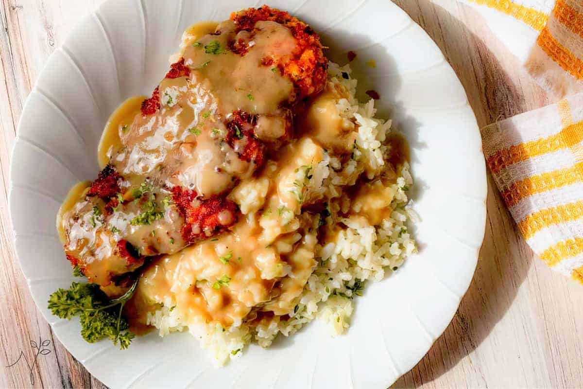 A plate of breaded chicken cutlets topped with savory gravy, served over rice and garnished with parsley.