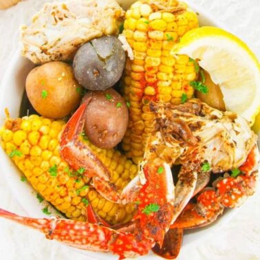A bowl featuring crab legs, corn on the cob, whole potatoes, a lemon wedge, and fresh herbsโperfect for seafood lovers craving bold ocean flavor.