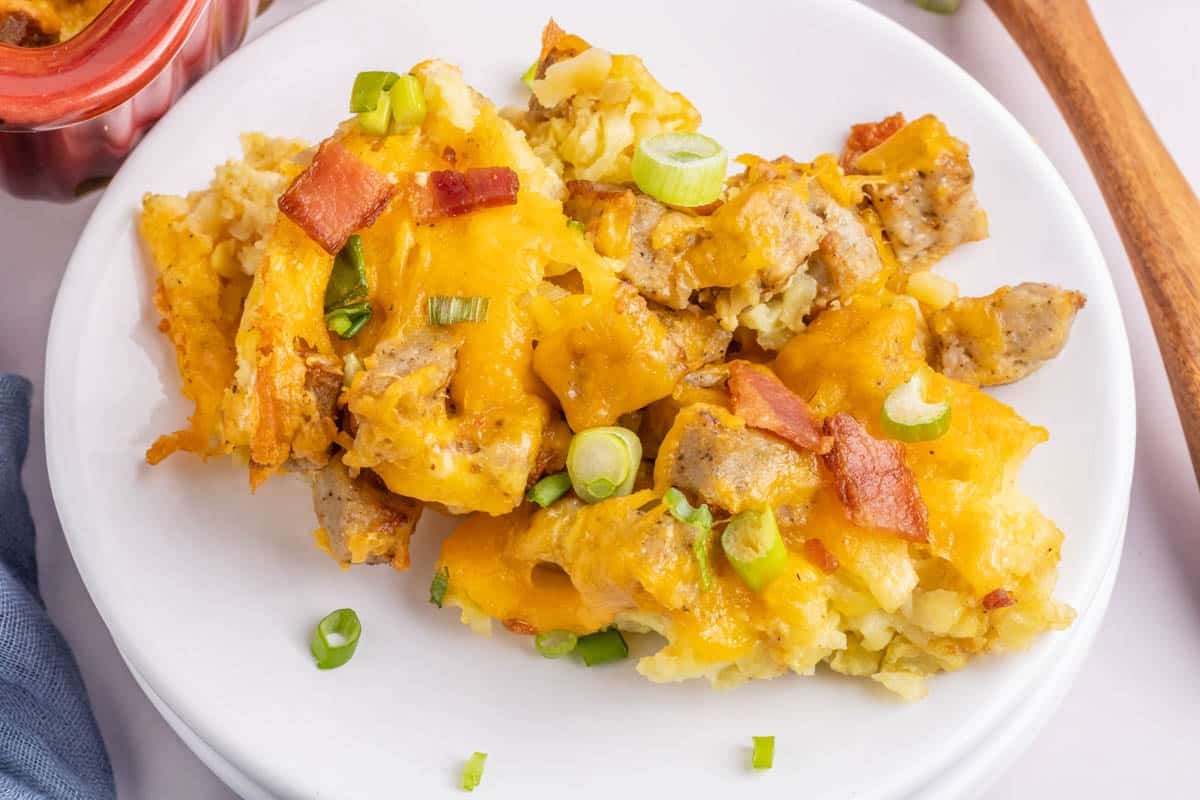 A serving of tater tot breakfast casserole with cheese, sausage, bacon, and chopped green onions on a white plate.