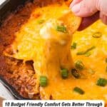 A hand dips a chip into cheesy, baked ground beef in a skillet, topped with melted cheese and green onions.