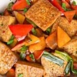 A bowl of stir-fried tofu with red bell peppers, green onions, and carrots, topped with a glossy savory sauce.