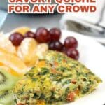 A slice of vegetable quiche on a white plate, served with green melon slices, grapes, and orange segments.