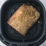 A seasoned piece of meat placed inside an air fryer basket on a marble countertop.