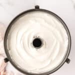 Overhead view of an unbaked angel food cake batter in a round tube pan on a white marble surface.