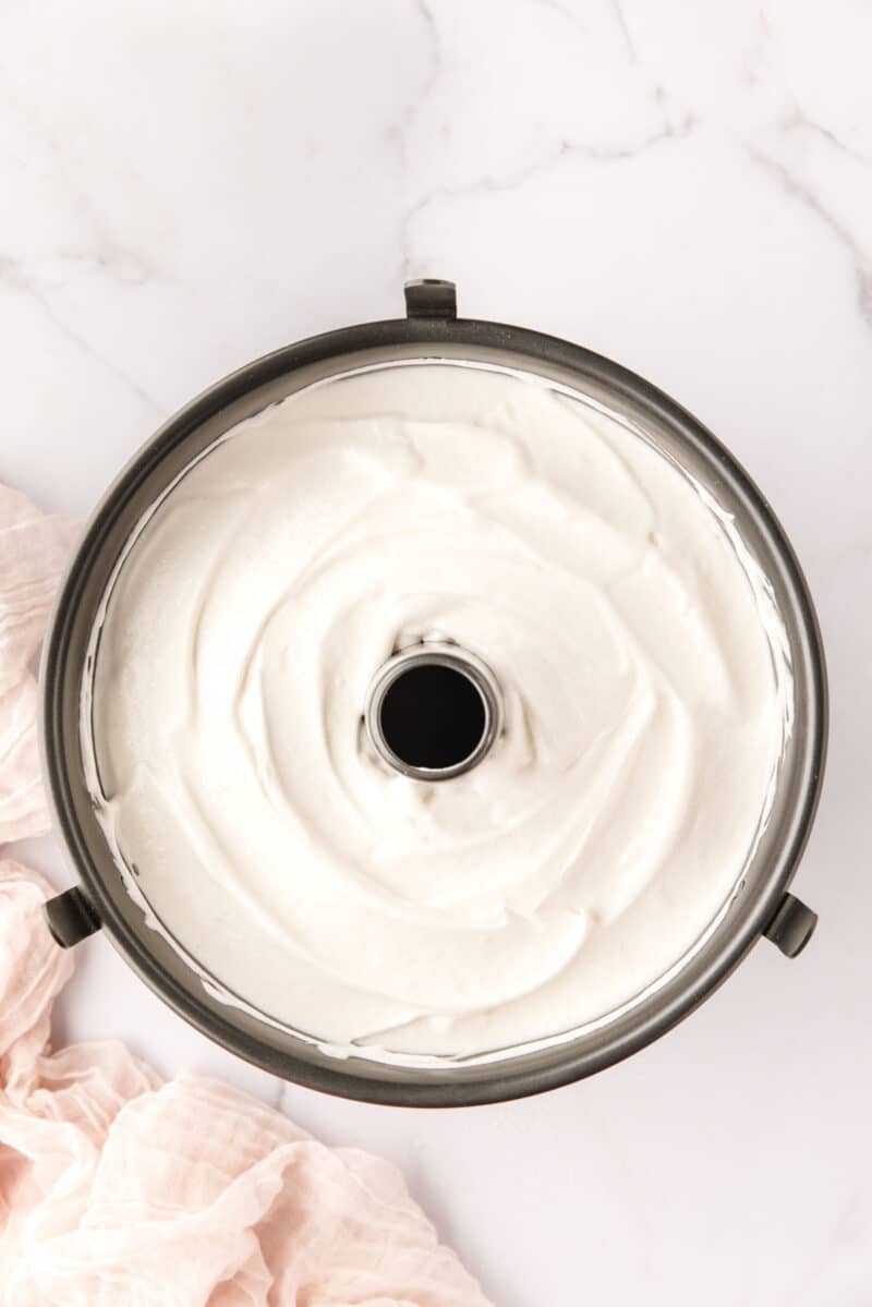 Overhead view of an unbaked angel food cake batter in a round tube pan on a white marble surface.