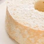 A plain angel food cake dusted with powdered sugar, displayed on a white plate.