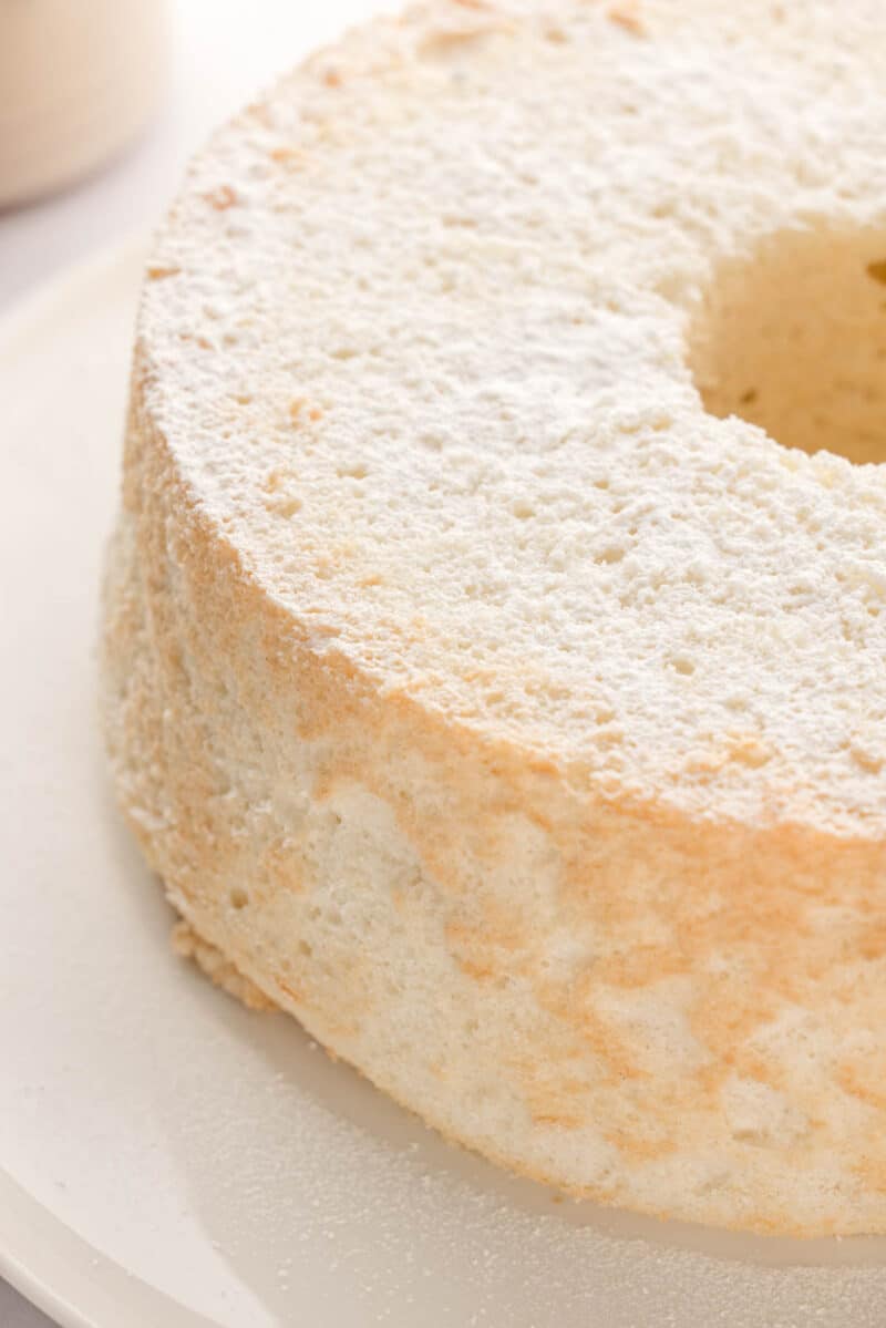 A plain angel food cake dusted with powdered sugar, displayed on a white plate.