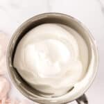 A metal mixing bowl filled with stiffly whipped egg whites sits on a white marble surface next to a light pink cloth.