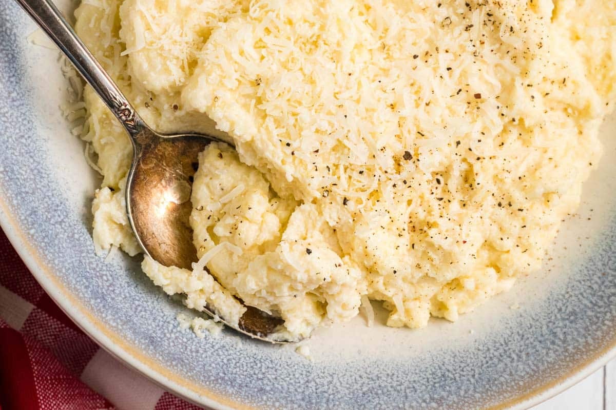 A plate of baked polenta topped with grated cheese and black pepper, with a spoon resting on the side.
