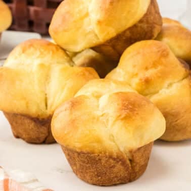 A close-up of several golden brown cloverleaf dinner rolls arranged on a white surface with a striped towel nearby.