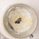 A mixing bowl containing flour, sugar, butter, and vanilla extract, partially mixed, on a light countertop with a cloth nearby.