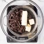 Chopped dark chocolate and blocks of butter in a metal bowl set over a pot of hot water on an electric stovetop, prepared for melting.