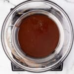 A glass bowl filled with melted chocolate sits over a saucepan on a marble countertop, viewed from above.