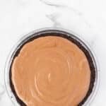 A chocolate pie with a smooth, swirled filling in a chocolate cookie crust sits on a white marble surface.