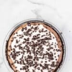 A chocolate cream pie with a whipped topping and chocolate chips, displayed in a glass pie dish on a white marble surface.