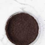 A glass pie dish filled with a pressed chocolate cookie crumb crust on a white marble surface.