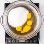 A bowl of eggs and sugar on a stove.