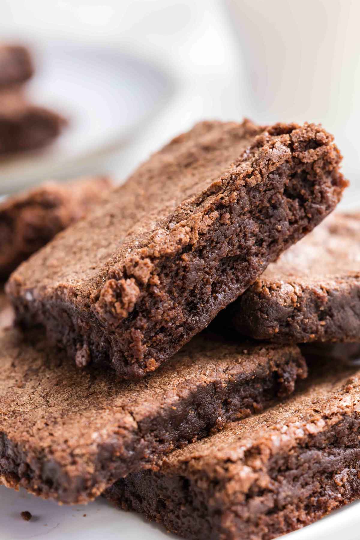 Close-up of several chocolate brownies stacked on a white plate, showing their moist and crumbly texture.