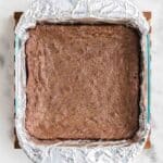 A square baking pan lined with aluminum foil containing a batch of baked brownies on a marble surface.