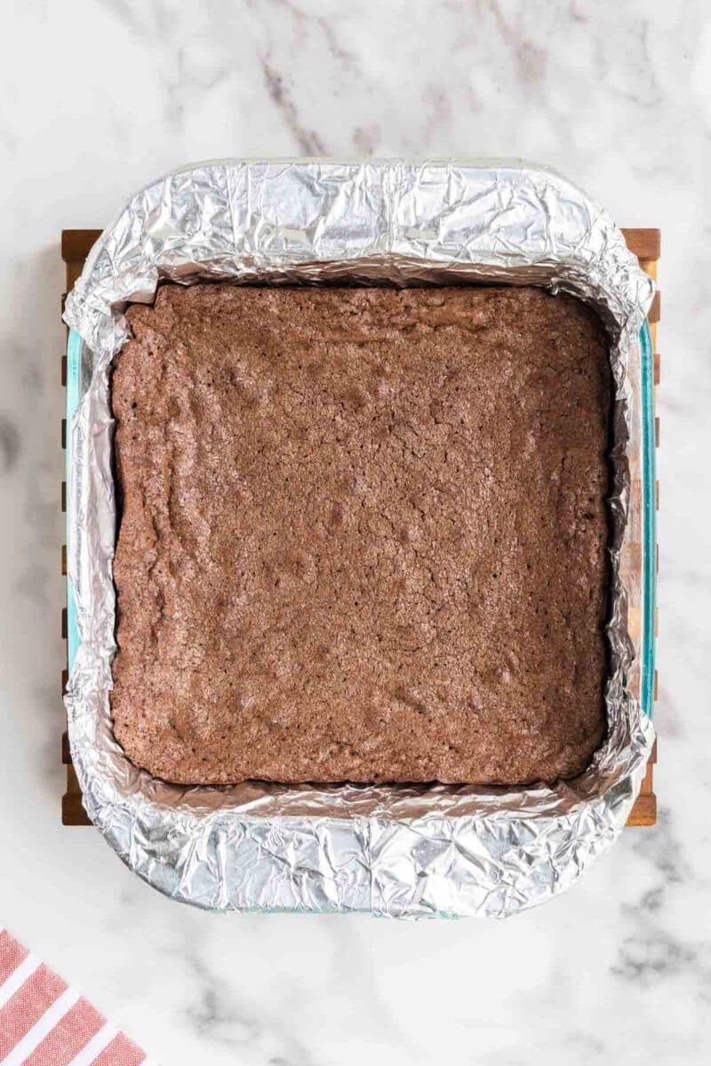 A square baking pan lined with aluminum foil containing a batch of baked brownies on a marble surface.