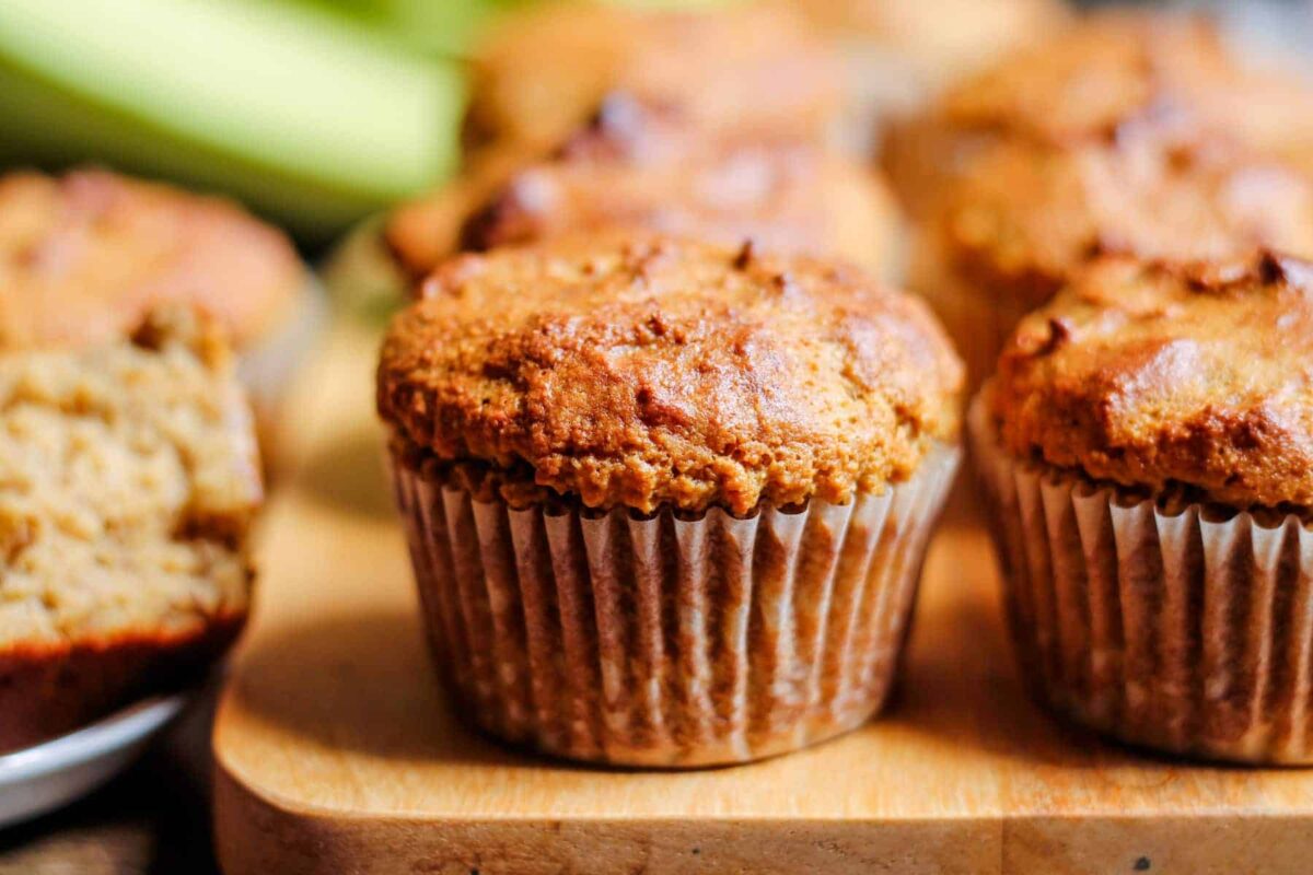 Close-up of several baked muffins in paper liners on a wooden board, with one muffin partially cut open in the background—perfect high energy bites for those seeking easy protein snacks.
