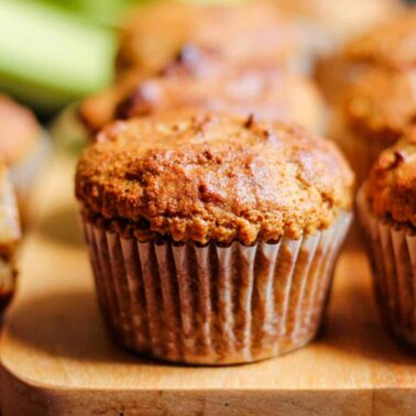 Close-up of several baked muffins in paper liners on a wooden board, with one muffin partially cut open in the backgroundโperfect high energy bites for those seeking easy protein snacks.
