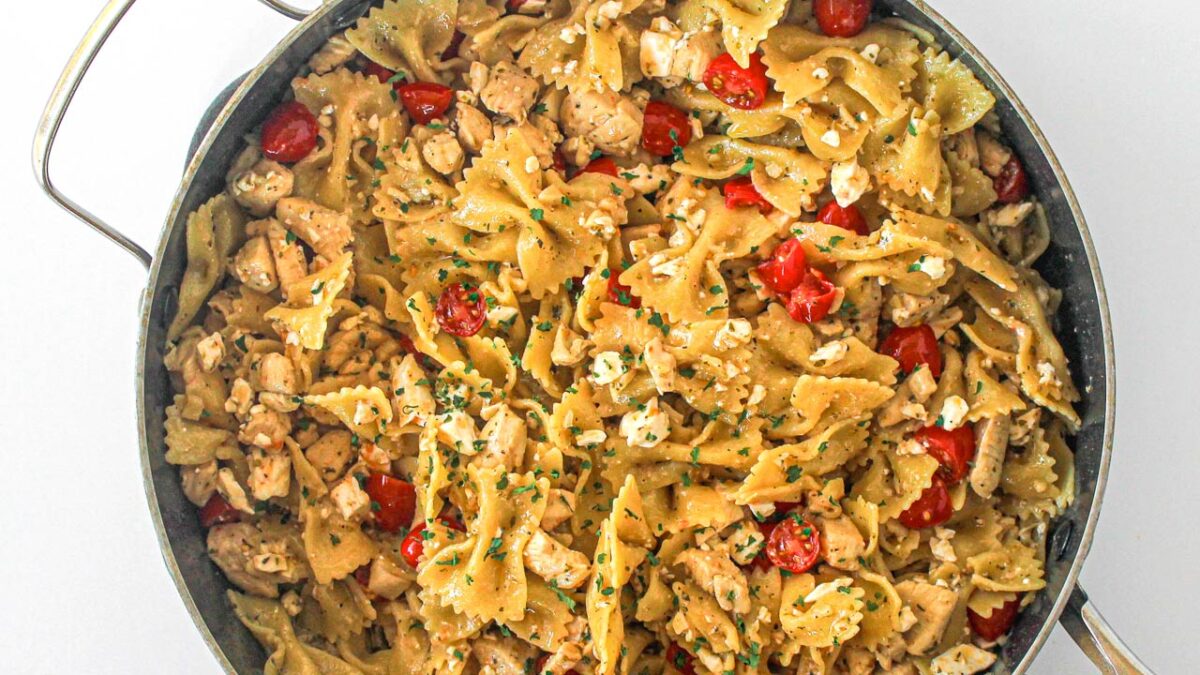 A skillet filled with bowtie pasta, diced chicken for extra protein, cherry tomatoes, crumbled cheese, and herbs.