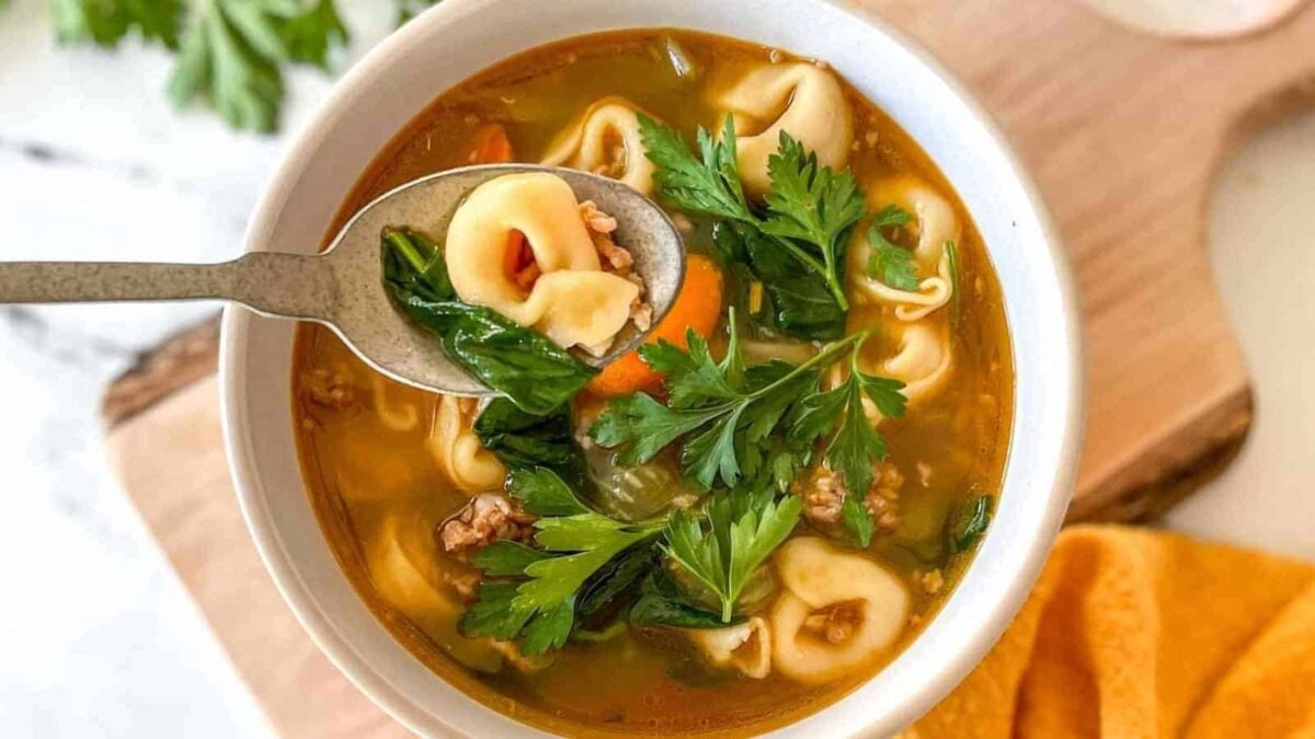 A bowl of soup with tortellini, leafy greens, carrots, and parsley, with a spoon lifting a portion from the bowl—one of those flavorful meals perfect for fast meals or easy Instant Pot recipes.