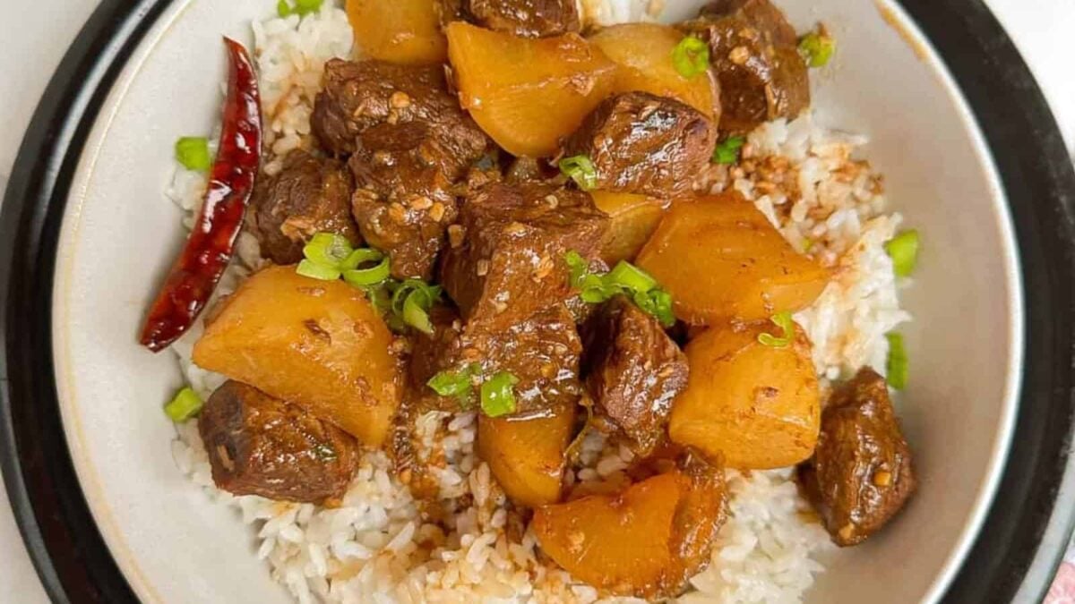 A bowl of white rice topped with slow simmered braised beef chunks, potatoes, green onions, a dried red chili, and savory sauce&mdash;a perfect choice for fans of cozy bowls and comforting meals.