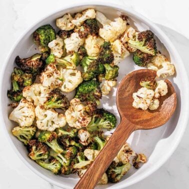 A white bowl filled with roasted broccoli and cauliflower florets, perfect for low carb sides, with a wooden spoon resting on the side.
