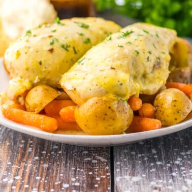 A plate with seasoned chicken breasts, baby potatoes, and baby carrots, garnished with herbsโperfect for fans of easy ranch recipes and creamy flavor pops.