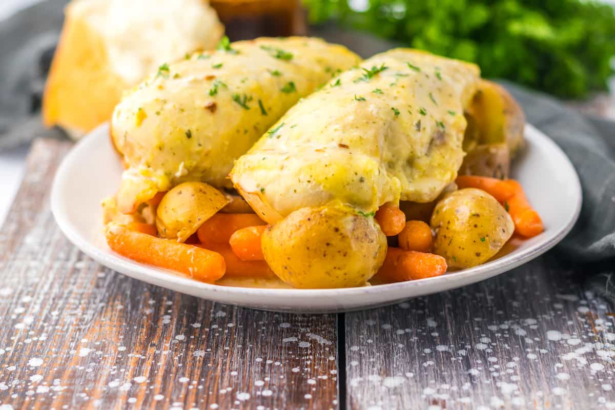 A plate with seasoned chicken breasts, baby potatoes, and baby carrots, garnished with herbs—perfect for fans of easy ranch recipes and creamy flavor pops.