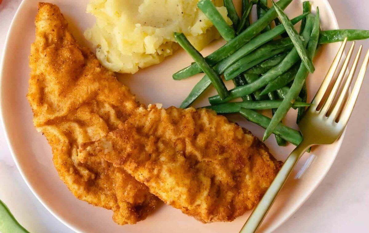 A plate with two breaded chicken tenders, mashed potatoes, green beans, and a gold fork—perfect for satisfying classic cravings with a comforting at-home meal.