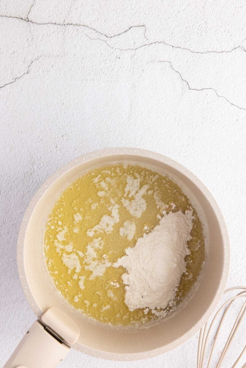 A saucepan containing melted butter with a mound of flour on top, ready to be mixed, sits on a light-colored surface.