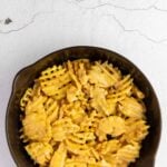 A cast iron skillet filled with waffle fries covered in melted cheese, placed on a light-colored, textured surface.
