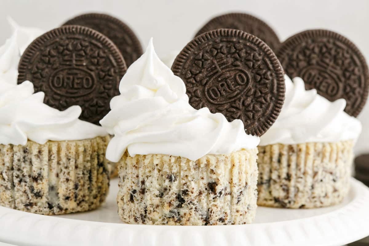 Cupcakes with cookies and cream pieces, topped with swirls of white frosting and whole Oreo cookies, arranged on a white plate.