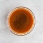 A clear glass bowl filled with a dark brown liquid sits on a light-colored marble surface.