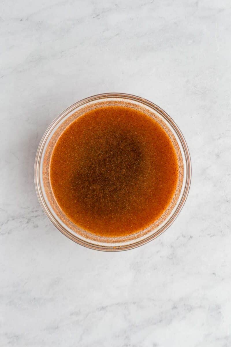 A clear glass bowl filled with a dark brown liquid sits on a light-colored marble surface.