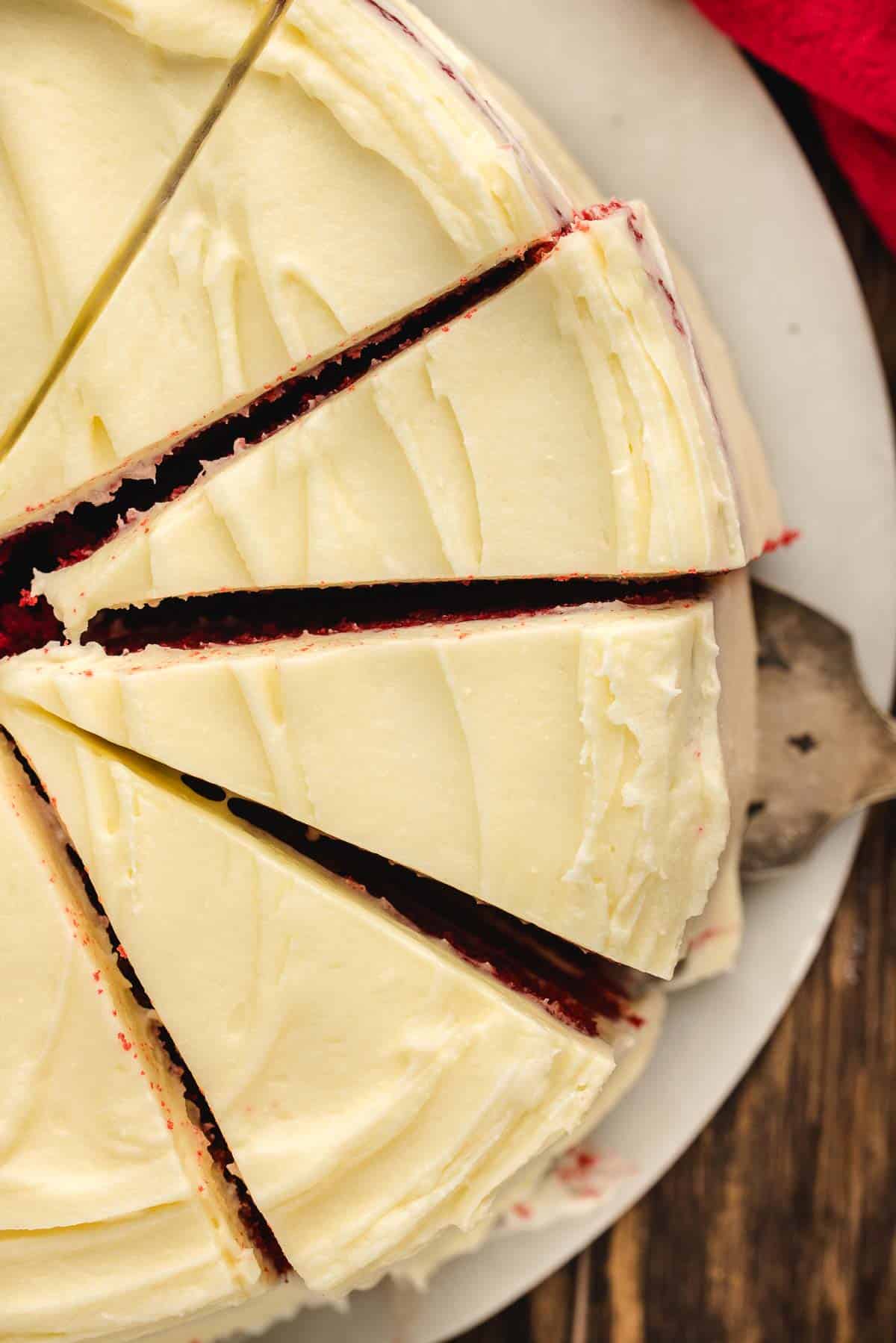 A sliced red velvet cake with cream cheese frosting on a white plate, viewed from above.