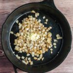 Diced onions and minced garlic are sautéing in a black cast iron skillet on a wooden surface.
