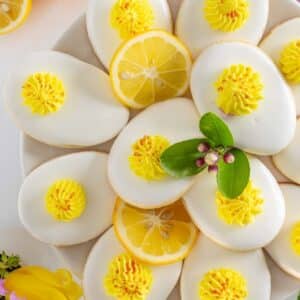 Plate of oval cookies with white icing and yellow frosting, garnished with lemon slices and a green leaf.