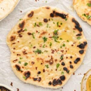 A piece of naan bread garnished with chopped herbs and red pepper flakes, placed on parchment paper.
