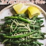 A plate of fresh green beans topped with shredded cheese, served with lemon wedges on the side.