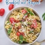 A bowl of pasta salad with bacon, tomatoes, spinach, and shredded cheese sits on a table next to a gold fork. Text reads: "16 Bacon Recipes That Add Smoky Flavor to Breakfast and Beyond.