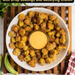 A plate of fried okra with crisp coatings surrounds a bowl of dipping sauce, set on a wooden trivet with parsley and fresh okra nearby. Text reads, โ15 Fried Recipes with Crisp Coatings and Satisfying Crunch.โ.