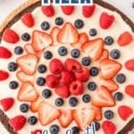 A brownie pizza topped with white frosting, sliced strawberries, blueberries, and raspberries, arranged in concentric circles.