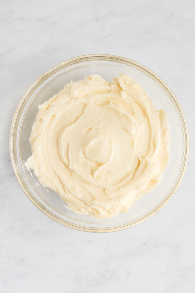 A glass bowl filled with smooth, creamy mashed potatoes on a light marble surface.
