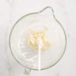 A glass mixing bowl containing a small amount of creamed mixture with a white spatula resting inside, on a white marble surface.