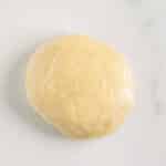 A ball of dough wrapped in plastic wrap on a white marble surface.