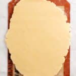 Rolled-out cookie dough on a silicone baking mat over a marble surface, with some scattered flour visible in the corner.